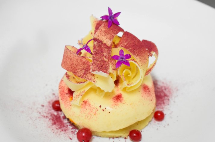 A plated dessert features a creamy, layered confection topped with edible garnishes and sprinkles of saffron.