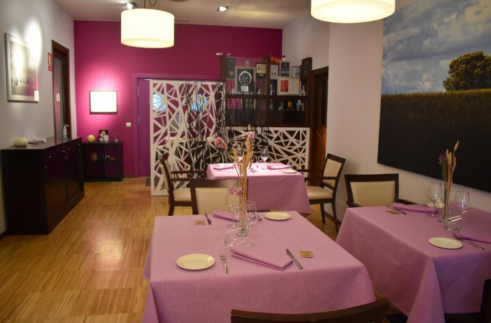 A well-lit interior of Azafrán restaurant's dining room features tables set with pink tablecloths and wooden seats.  