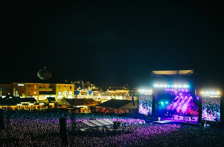 Large crowd gathers at outdoor music festival Country Calling by the waterfront, with a brightly lit stage and surrounding buildings at night.