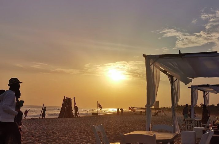 A serene sunset at a vibrant Ghanaian beach, dotted with visitors, cozy seating, and a calm ambiance.