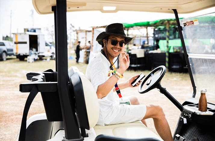 A man wearing a hat and sunglasses is seated in a golf cart at the Wonderfruit festival, Thailand.