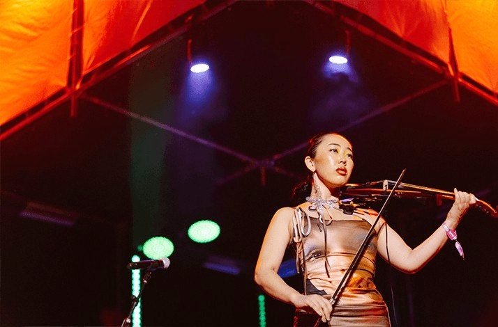 Violinist performing on stage under vibrant lights at Wonderfruit festival in Thailand.