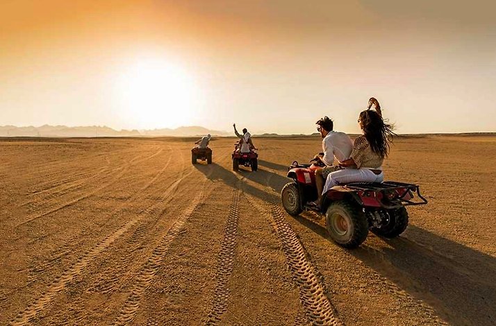 A convoy of quad bikes traversing across a vast desert trails during the golden hour at Agafay Desert.