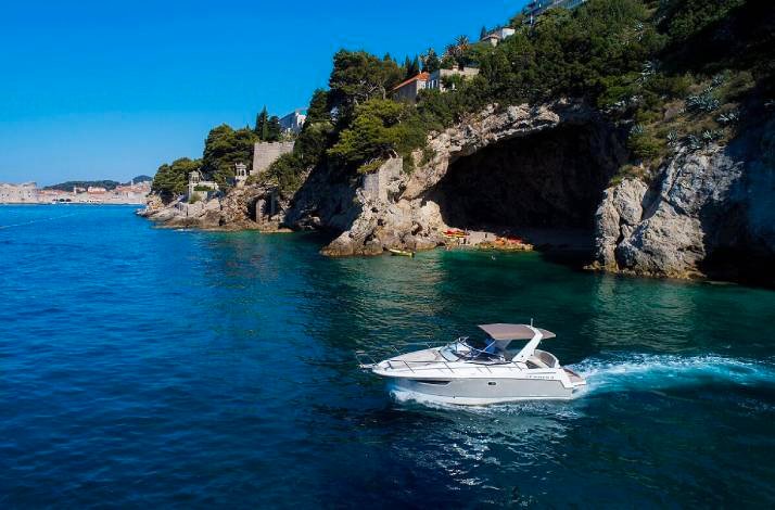 Private motorboat navigating clear teal waters beside rugged sea cliffs near Dubrovnik's historic waterfront, Croatia.