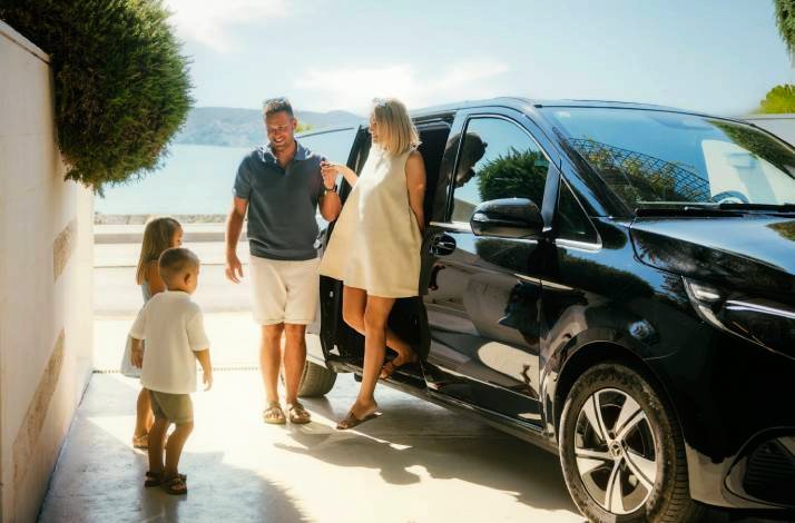 Couple with two young children stepping out of a black premium SUV at a sun-drenched Croatian coastal property. 