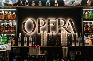 A sleek bar display with OPERA illuminated, surrounded by premium liquor bottles.