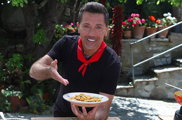 Celebrity chef Gino D'Acampo presenting a dish outdoors.