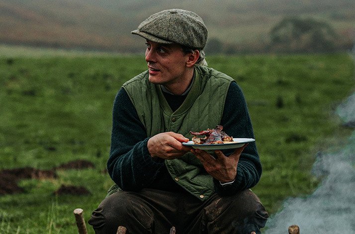 Celebrity chef Thomas Straker holding a plate of food in a field.