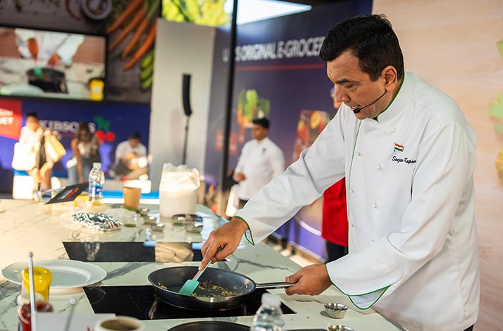 Chef in white coat prepares food in a pan at a live cooking demonstration