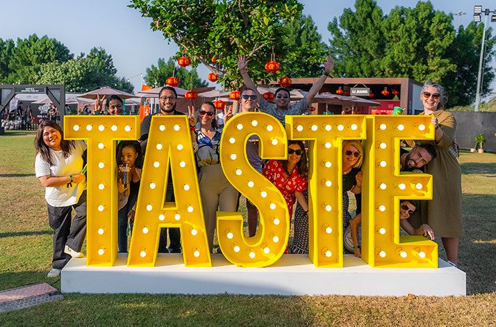 A group of people posing behind large yellow TASTE letters.