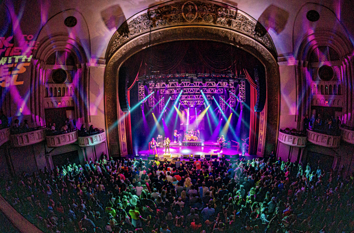 A large crowd in a full theatre enjoying a live performance and light show.
