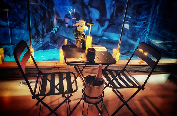 A romantic, dimly lit setting with a small table set for two, and a backdrop that suggests an icy cavern at Calumet Falls