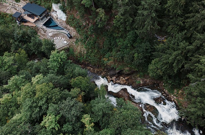 An aerial view of a secluded lodge built into a hillside, with a rushing waterfall cascading down a gorge at Calumet Falls