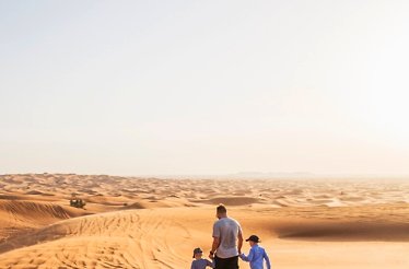 A parent with two children walking in the sandy desert.