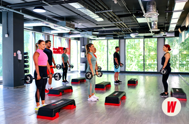 A group of people are holding barbells and working out in a fitness class, with a trainer at World Class Romania gym 
