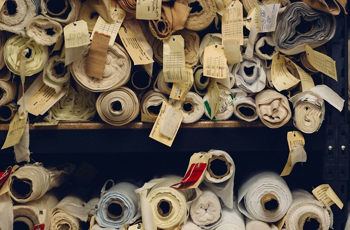 Rolls of fabric with tags, stored on shelves in a costume workshop.