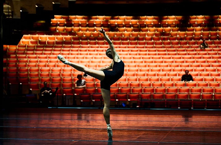 Ballet dancer performing on stage with empty orange seats in the background.