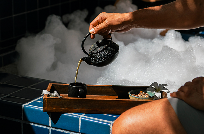 A hand pouring tea from a black teapot into a small cup, offered at Hotel El Ganzo