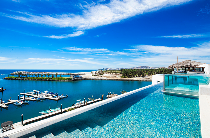 A view of a pool overlooking a coastal marina, under a vibrant blue sky at Hotel El Ganzo