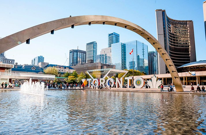 Nathan Phillips Square in Toronto, featuring the 'TORONTO' sign, a reflecting pool, and a backdrop of modern skyscrapers 
