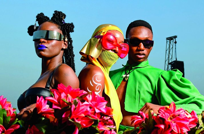 Close-up shot showcases three individuals posing in a bright outdoor setting, each with distinct styles and accessories.