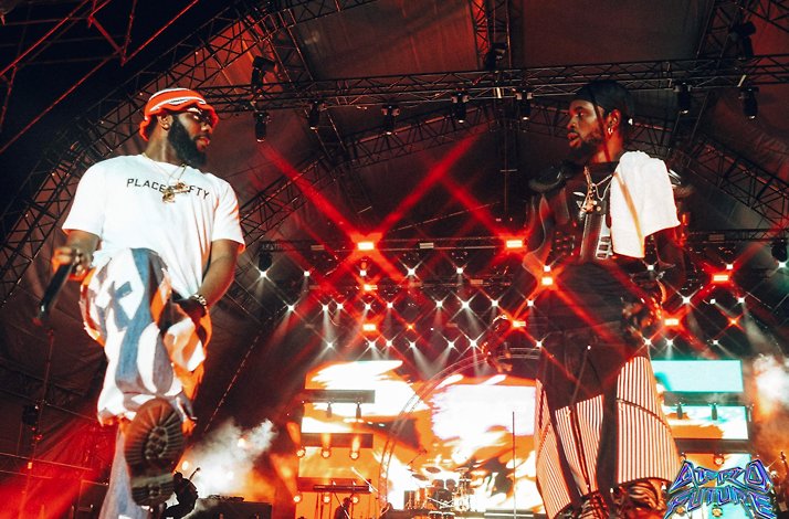 Mid-concert moment, featuring two performers on stage under dramatic lighting, entertaining the crowd at El Wak Stadium.