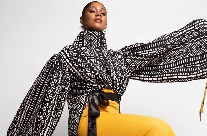  A woman wearing a black and white printed jacket paired with bright yellow pants stands confidently.