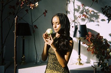A young lady holding a flower to feel the scent in a dim room.