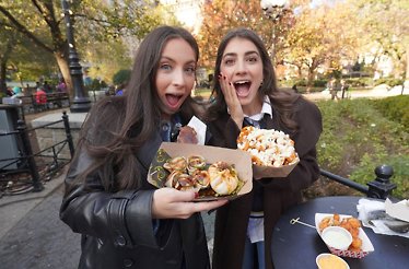 Sistersnacking sisters holding carton baskets with New York City snacks.