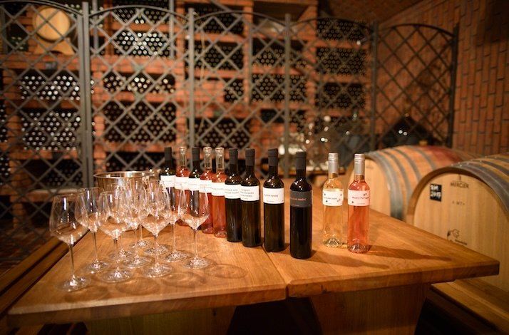 Wine bottles and glasses arranged on a wooden table inside the cellar at St. Claire’s Vineyard.