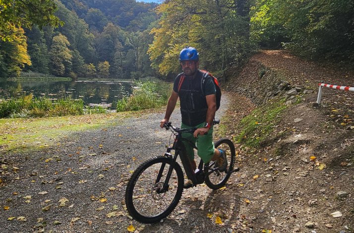 A lone rider pauses by a tranquil pond surrounded by rich autumn foliage on a gravel path.