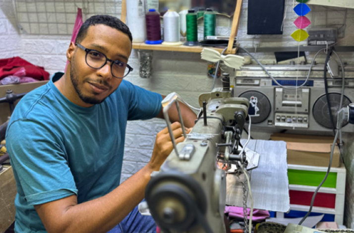 A man in a blue shirt operates a sewing machine, focused on his task.