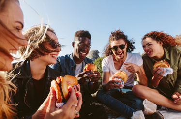 Group of friends sitting outdoors on a sunny day, eating burgers together
