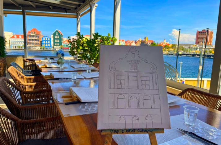 Canvas with a Curacao building sketch set up for painting, overlooking the colorful waterfront skyline.