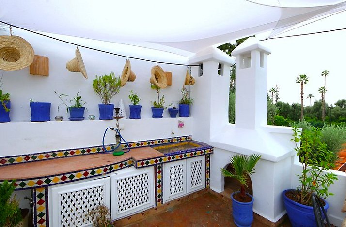 Part of the outdoor lounge/dining area of the Riad Elli Marrakech hotel with a lot of potted plants and colorful counter against white walls.