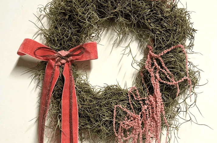 A Spanish moss wreath decorated with a pink velvet ribbon and dried pink flowers