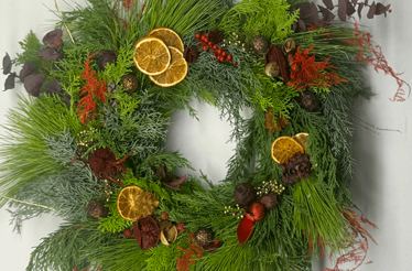 A decorated Christmas wreath, featuring various types of evergreen branches, dried orange slices and pinecones,