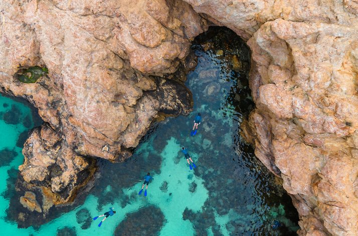 View from the top on people snorkeling beneath dramatic cliffs.