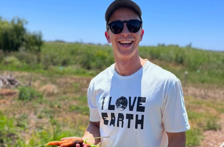 Person holding freshly picked carrots in a sunny vegetable garden.