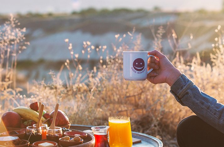 A tray with breakfast prepared by chefs from the Taskonaklar Hotel. Next to it a person with a hot cup of coffee in hand.