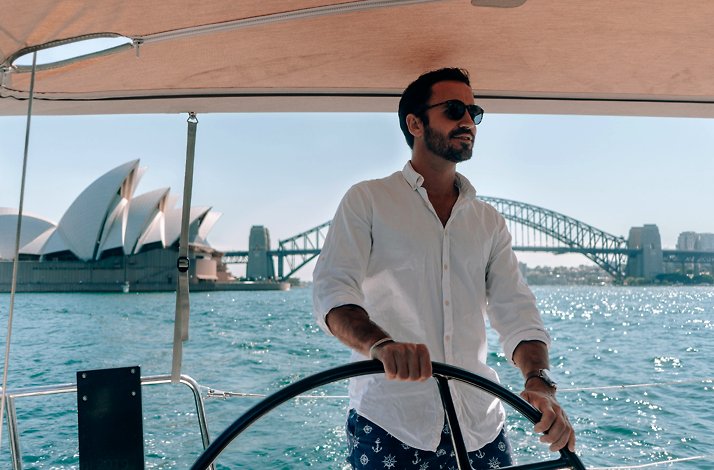 A man wearing sunglasses grabbing the steering wheel of a private yacht in the Sydney Harbour.