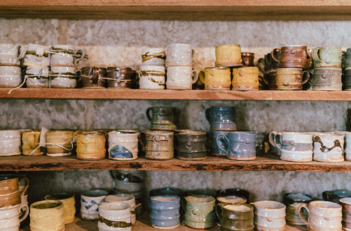 Collection of handmade ceramic mugs and pottery items displayed on wooden shelves.