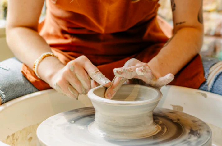 A person is shaping wet clay into a pot on a spinning potter's wheel.