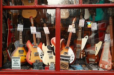 Vintage electric guitars with price tags filling a red-framed shop window on Denmark Street, London.