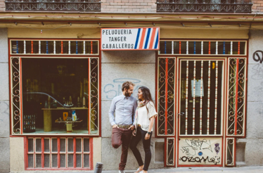 A couple standing in front of a traditional Spanish barbershop called 'Peluquería Tánger Caballeros'