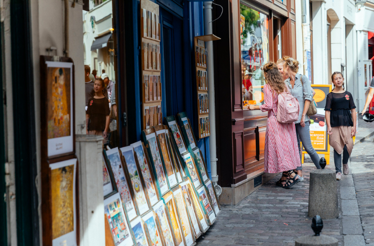 A street scene in Paris, featuring people interacting near shops adorned with art, creating a lively square