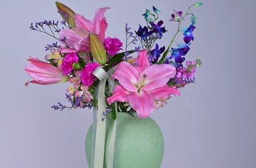 Green vase with pink lilies and purple flowers.