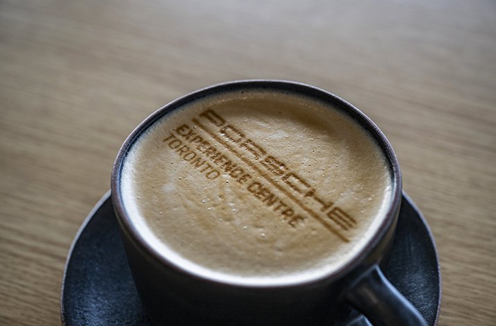 A cup of cappuccino with Porsche Experience Centre Toronto logo drafted drawn with cinnamon powder.