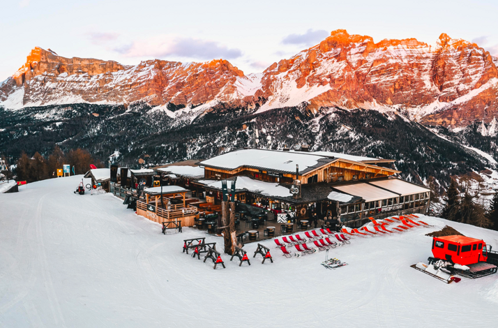 Aerial shot showcases Club Moritzino on Piz La Ila at sunset, dominated by its wooden lodge and its surrounding structures.