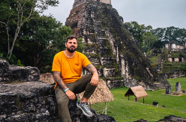 Kristijan Iličić sitting on stone ruins in front of an ancient pyramid at an archaeological site